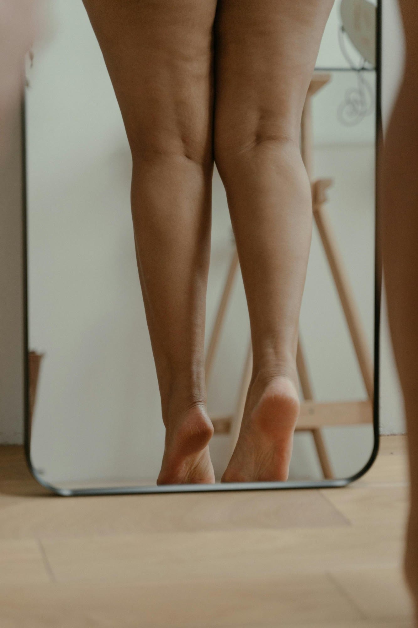 Pernas de uma mulher refletidas em um espelho apoiado no chão, em casa